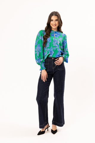 Woman wearing a green and blue floral print blouse with navy wide-leg jeans and black heels.