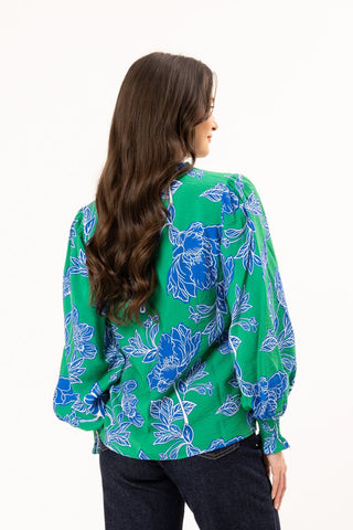 Woman from behind wearing a green floral print long sleeve blouse and dark jeans
