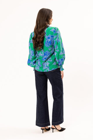 Woman wearing a green and blue floral print blouse with dark wash wide-leg jeans.
