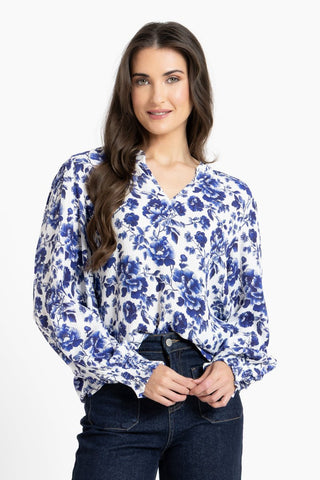 Woman wearing a white and blue floral print blouse paired with dark blue jeans.
