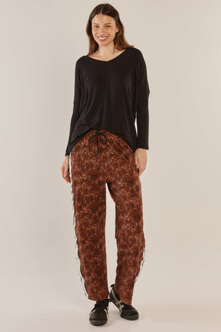 Woman wearing a black v-neck top and brown leopard print leisure pants with side stripes.