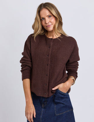 Woman wearing a brown ribbed button-up cardigan and a dark blue denim skirt.