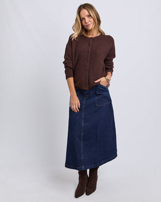 Woman wearing a brown ribbed cardigan, navy blue denim midi skirt, and brown ankle boots.