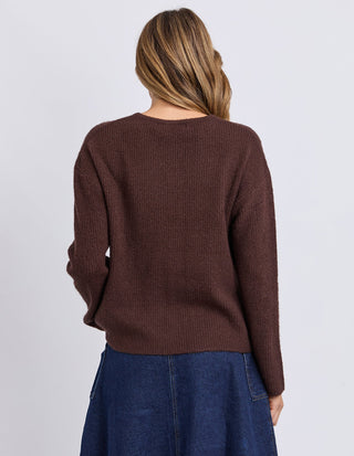 Back view of a woman wearing a brown ribbed knit sweater and a blue denim skirt