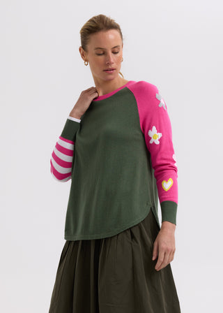 Woman wearing a green and pink color-block sweater with flower details and an olive skirt.
