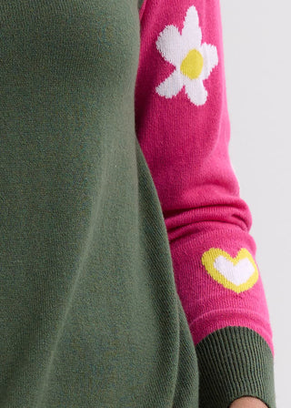 Close-up of an olive green sweater with a bright pink sleeve featuring a white flower and heart.
