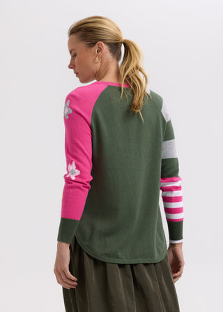 Woman in a color-block green and pink sweater with floral embroidery and a dark olive skirt