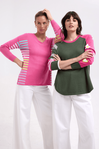 Two women wearing colorful long-sleeve knit sweaters and white wide-leg pants.
