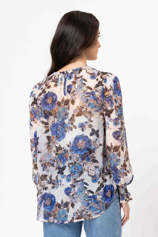 Back view of a woman wearing a blue and brown floral print long sleeve blouse and blue jeans.
