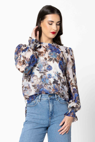 Woman wearing a blue and brown floral print blouse with light blue jeans.
