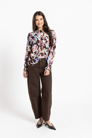 Woman wearing a multi-colored floral print blouse and brown wide-leg trousers.