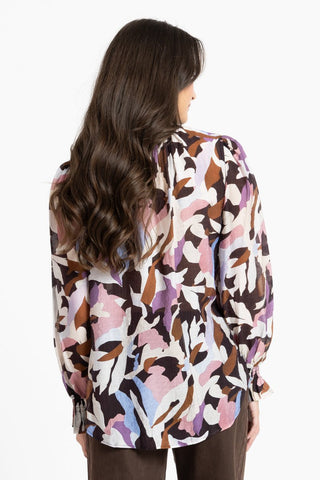 Back view of a woman wearing a multicolored abstract print long-sleeved blouse.