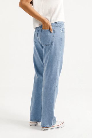 Side view of a woman wearing light wash wide leg denim jeans and white sneakers