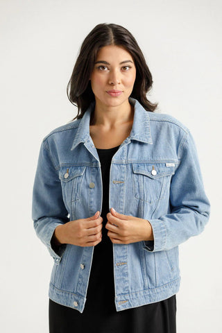 Woman wearing a light wash blue denim jacket over a black dress.