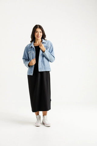 Woman wearing a light blue denim jacket over a long black dress and white sneakers