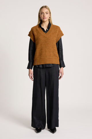Woman wearing a brown knitted vest over a black button-down shirt and wide-leg black trousers