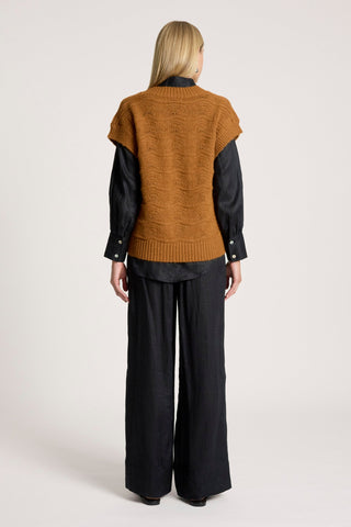 Woman from behind wearing a brown cable knit vest, black shirt, and wide leg trousers.