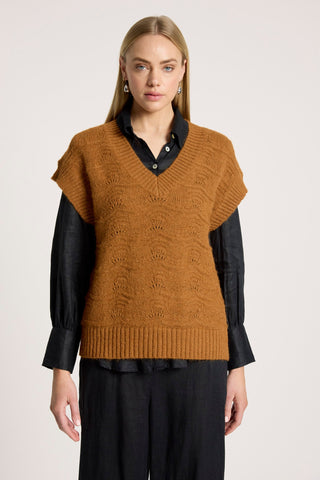 Woman wearing a brown knit sweater vest over a black button-down shirt and black pants.