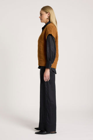Woman in a brown cable knit vest, navy blue long sleeve shirt, and wide leg navy trousers.