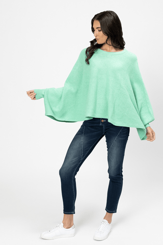 Woman wearing a mint green oversized knit poncho with dark blue skinny jeans and white sneakers