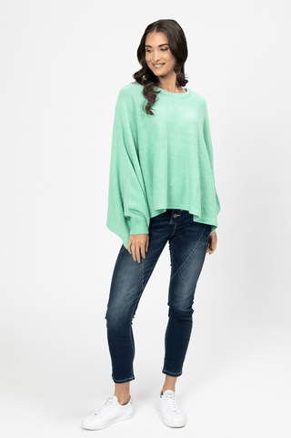 Woman wearing a mint green oversized knit sweater, dark blue skinny jeans, and white sneakers.