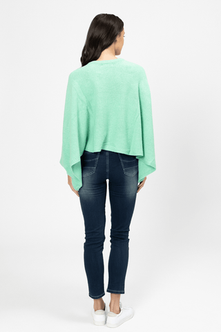 Back view of a woman wearing a mint green knit poncho and dark blue skinny jeans.