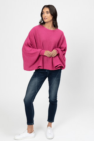 Woman wearing a bright pink oversized knit sweater with dark blue skinny jeans and white sneakers