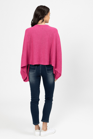 Woman from behind wearing a bright pink knit poncho and dark blue skinny jeans.