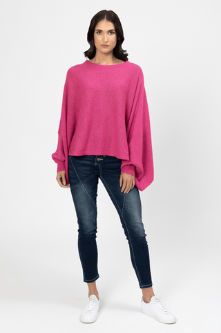 Woman wearing a bright pink oversized knit sweater, dark blue skinny jeans, and white sneakers.
