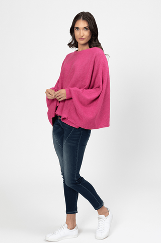 Woman wearing a bright pink oversized knit sweater, dark blue jeans, and white sneakers.