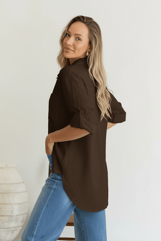 Woman wearing a chocolate brown button-up shirt and blue jeans.