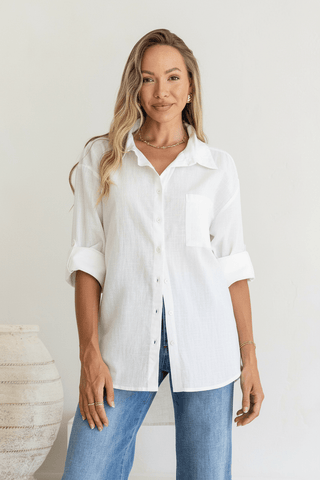 Woman wearing a white linen button-down shirt and blue jeans.