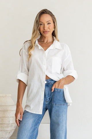 Woman wearing a white oversized linen shirt and blue wide-leg jeans.