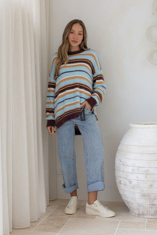 Woman wearing a multi-colored striped knit sweatshirt and light blue denim jeans.