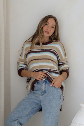 Woman wearing a striped fuzzy knit sweater and light wash denim jeans.