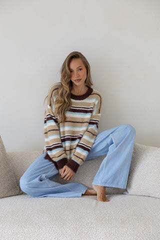 Woman wearing a striped fuzzy sweater and light blue wide-leg lounge pants sitting on a sofa.