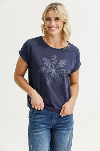Woman wearing a navy blue short sleeve t-shirt with a large white floral graphic and blue jeans.