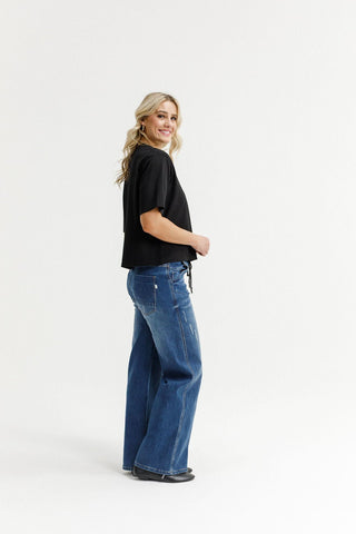 Woman smiling in a black t-shirt and blue wide-leg denim jeans.