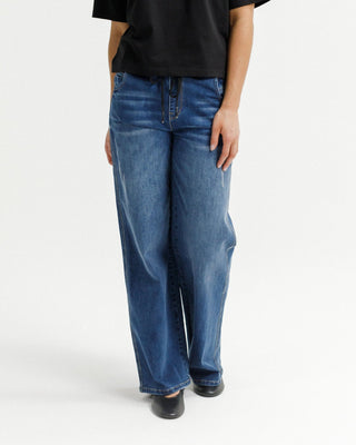 Woman wearing blue wide-leg denim jeans and black flats against a white background.
