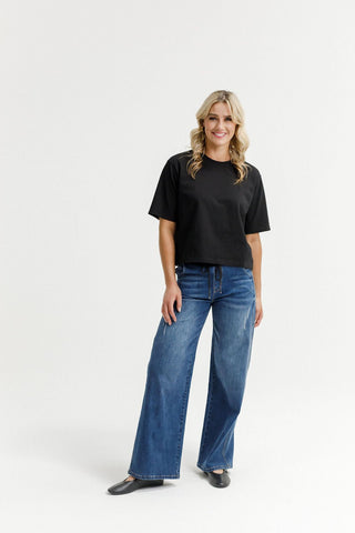 Woman wearing a black short sleeve t-shirt and blue wide leg denim pants.