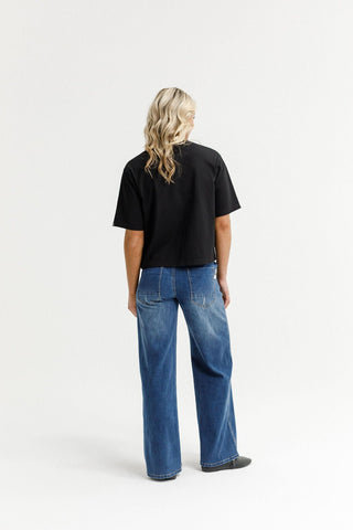 Woman wearing a black oversized t-shirt and blue wide-leg denim jeans from behind.