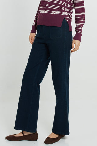 Woman wearing navy blue flared trousers, a striped maroon sweater, and brown flats.