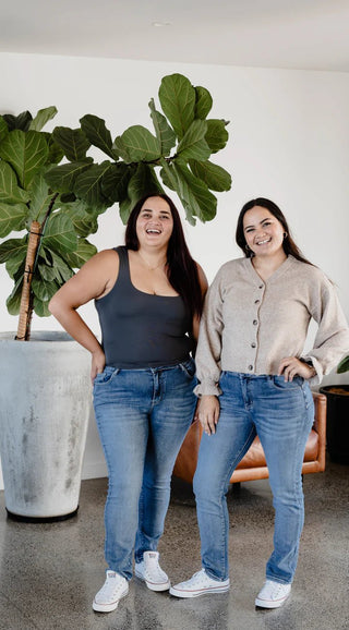 Two women smiling in casual lifestyle clothing, wearing tank tops, cardigans, and blue jeans.