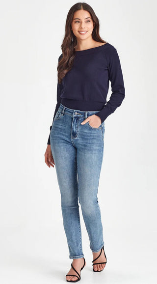 Woman wearing a navy blue off-the-shoulder long sleeve top and light wash blue jeans.