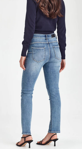 Back view of a woman wearing a navy long-sleeve top and blue slim-fit jeans with black heels.
