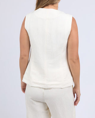 Back view of a woman wearing a white sleeveless linen vest and matching linen pants.