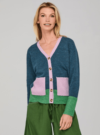 Woman wearing a blue, purple, and green color-block knit cardigan and green pants.