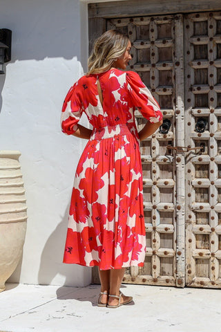 Woman wearing a red and white floral midi dress with puff sleeves standing by a wooden door.