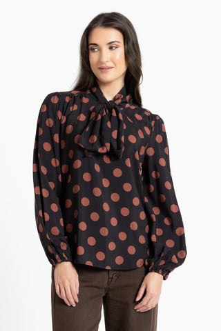 Woman wearing a black long sleeve blouse with large brown polka dots and a neck tie.