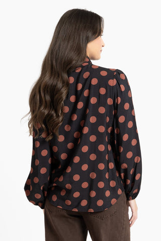 Woman wearing a black long-sleeve blouse with large brown polka dots.